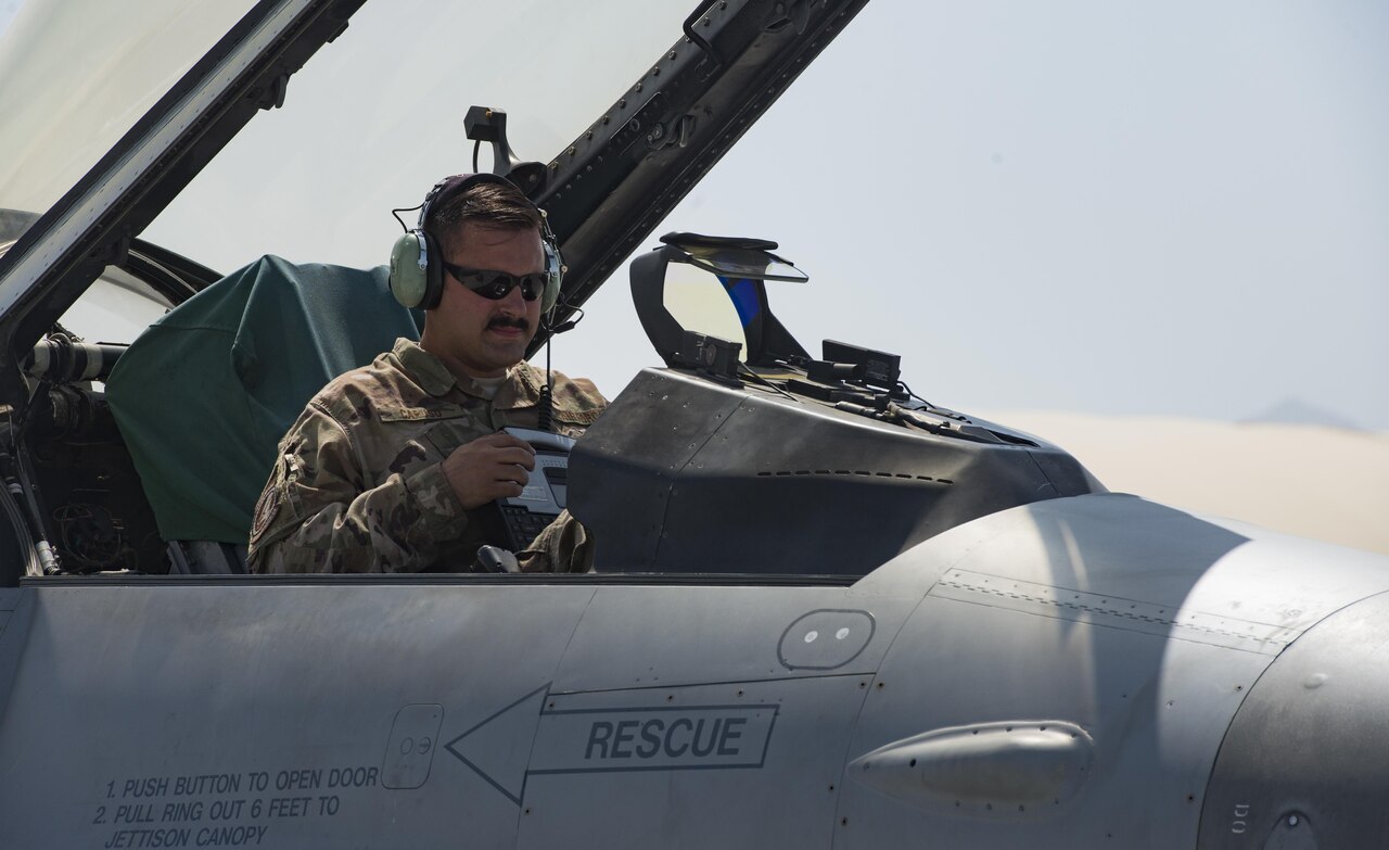 Airman sits in F-16 fighter jet cockpit to check equipment.
