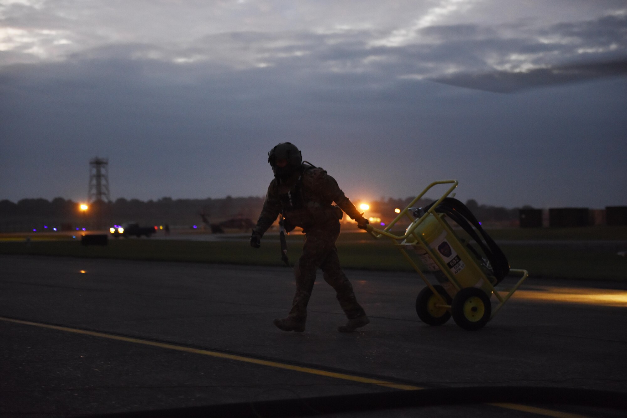 A staff sergeant who is an HH-60G Pave Hawk crewman from the 56th Rescue Squadron moves a fire extinguisher away from the helicopter taxi area at Royal Air Force Lakenheath, England, Oct. 26. The Pave Hawk helicopters are refueled while running to minimize time on the ground. (U.S. Air Force photo/ Airman 1st Class John A. Crawford)