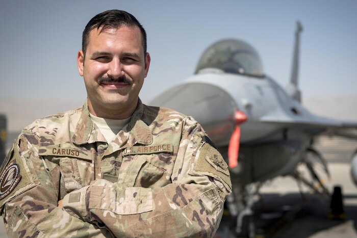 An airman stands in front of a military jet.