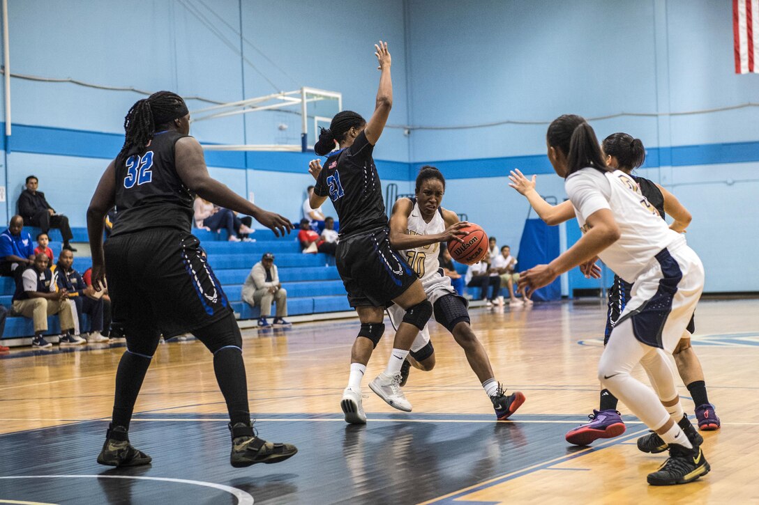 A sailor drives down the basketball court past a player trying to block her as others stand ready.