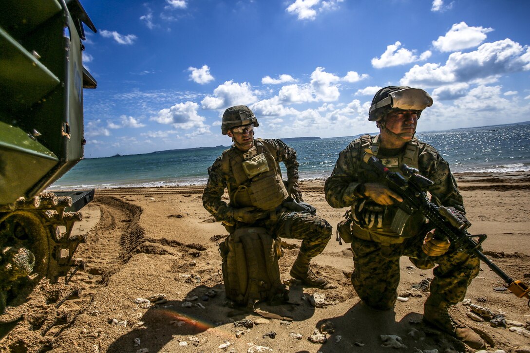 Two Marines kneel in the sand on a beach.