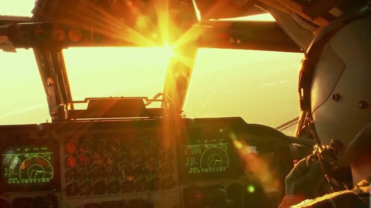 A service member flies a bomber with the sun in the background.