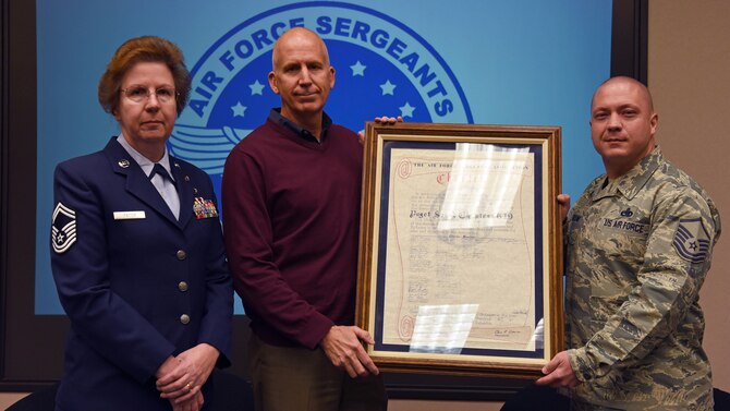 Senior Master Sgt. Carol Patten, Air Force Sergeants Association Chapter 1461 Executive Committee trustee, left; Cary Hatzinger, Chapter 1461 senior advisor, center; and Master Sgt. Kenneth Markline, Julius A. Kolb Airman Leadership School commandant, stand with the Chief Master Sgt. Thomas N. Barnes Air Force Sergeants Association Chapter 1461 original hand-scribed charter, Oct. 31, 2017 at McChord Field.