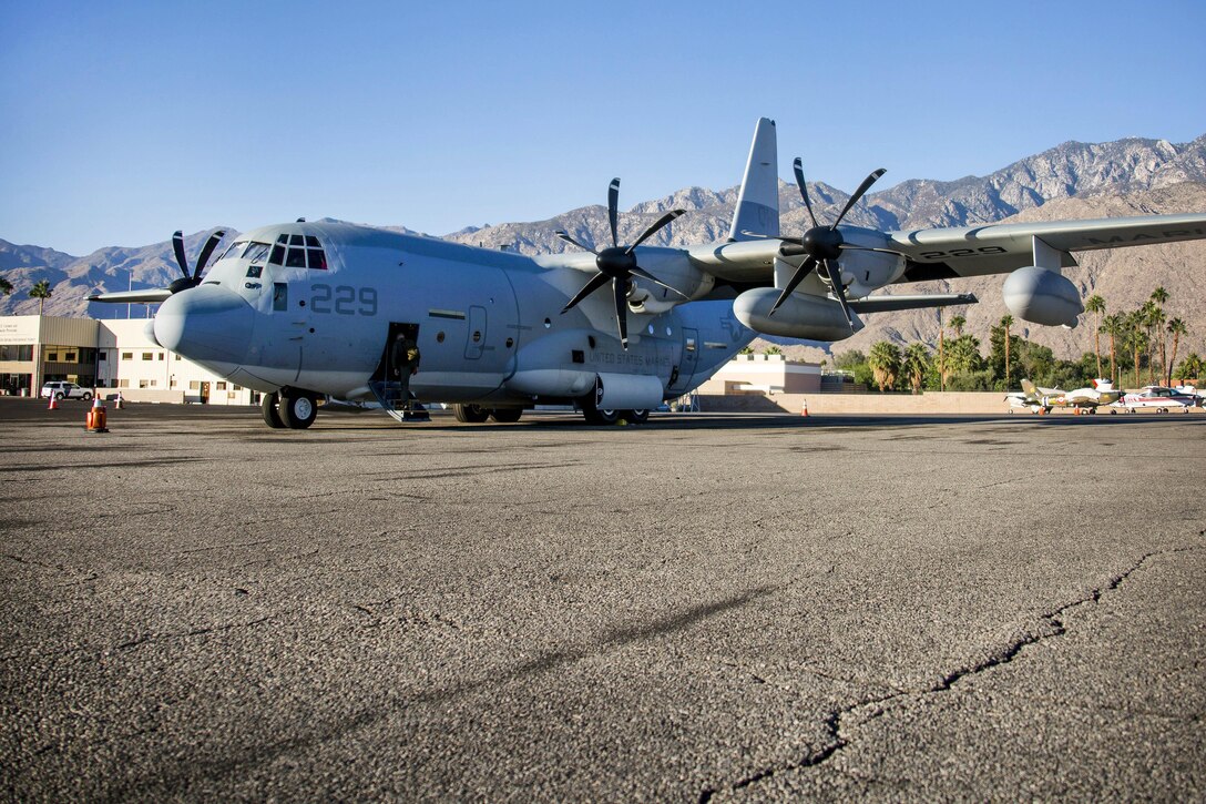 A KC-130J Super Hercules aircraft on a flight line with mountains in the background.