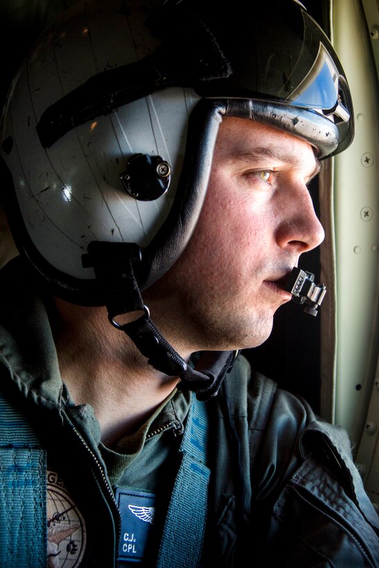 A Marine in a flight helmet looks out of an aircraft window.