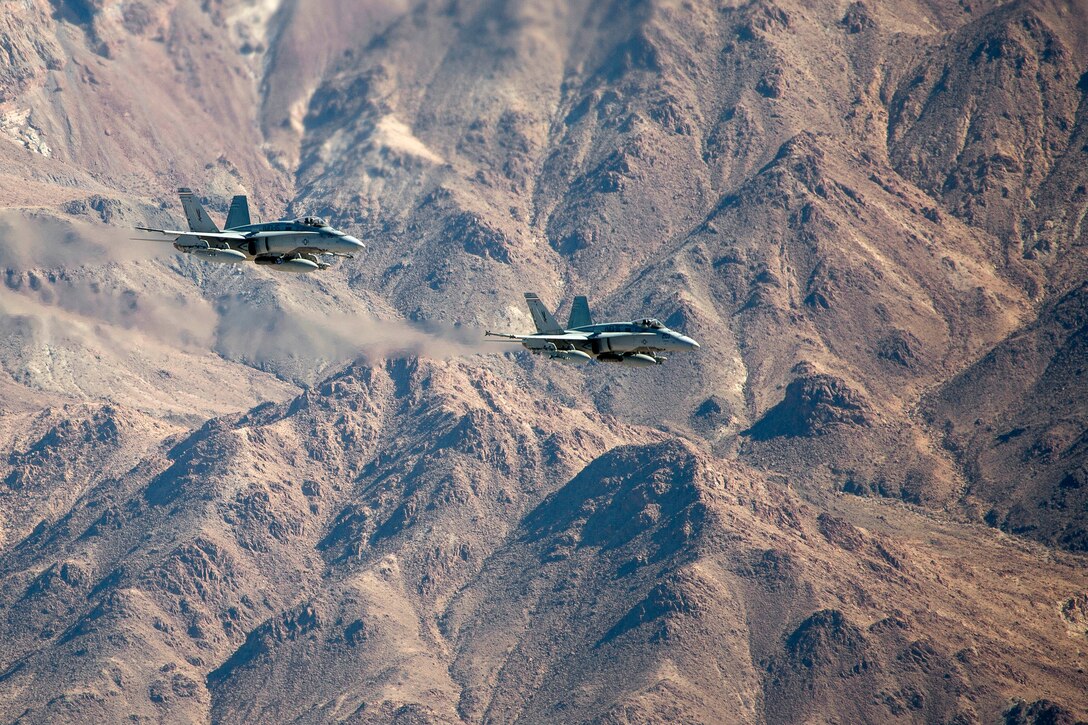 F/A-18C Hornet aircraft fly over mountains in the California desert.