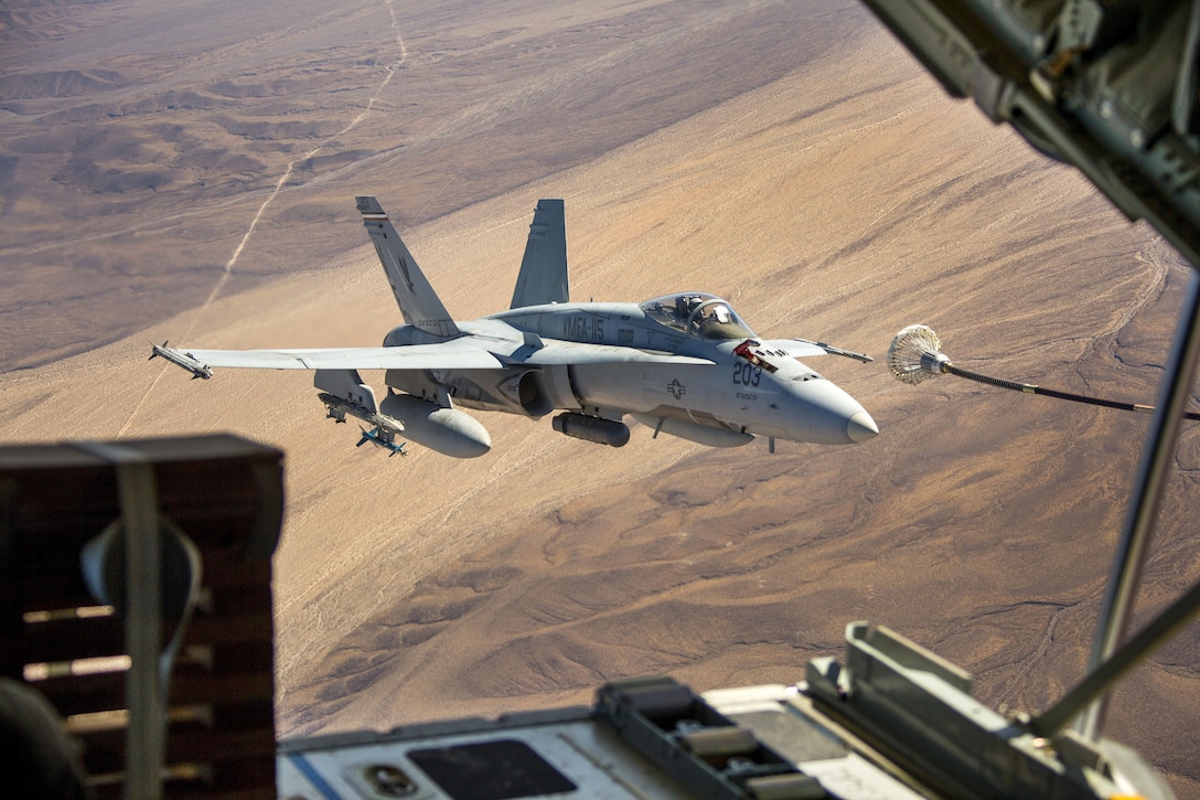 An F/A-18C Hornet flies over the California desert, framed by the tailgate of a C-130 Hercules while refueling.