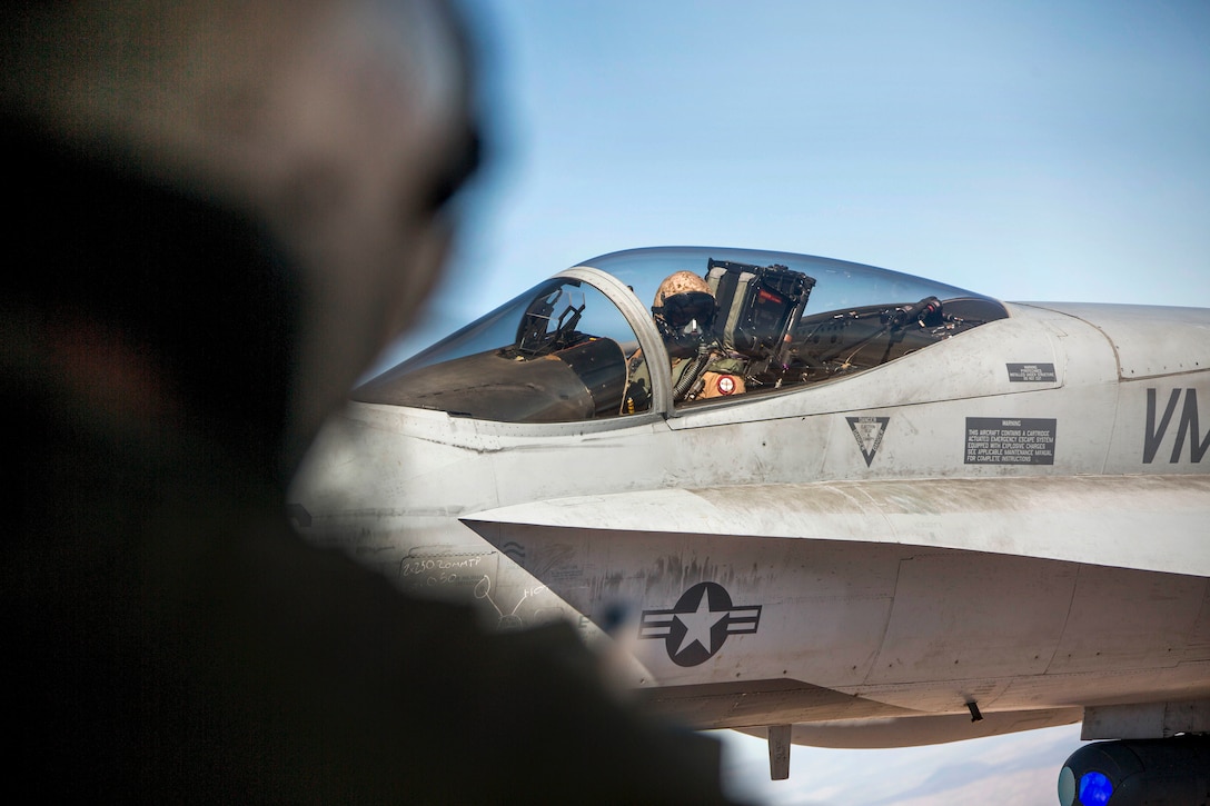 An F/A-18C Hornet pilot looks over at a KC-130J Super Hercules aircraft while conducting aerial refueling.