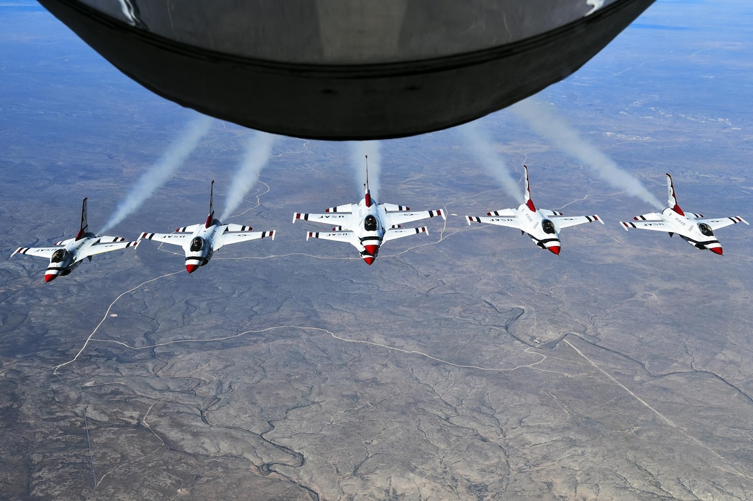 Six aircraft fly in formation under an aircraft boom.
