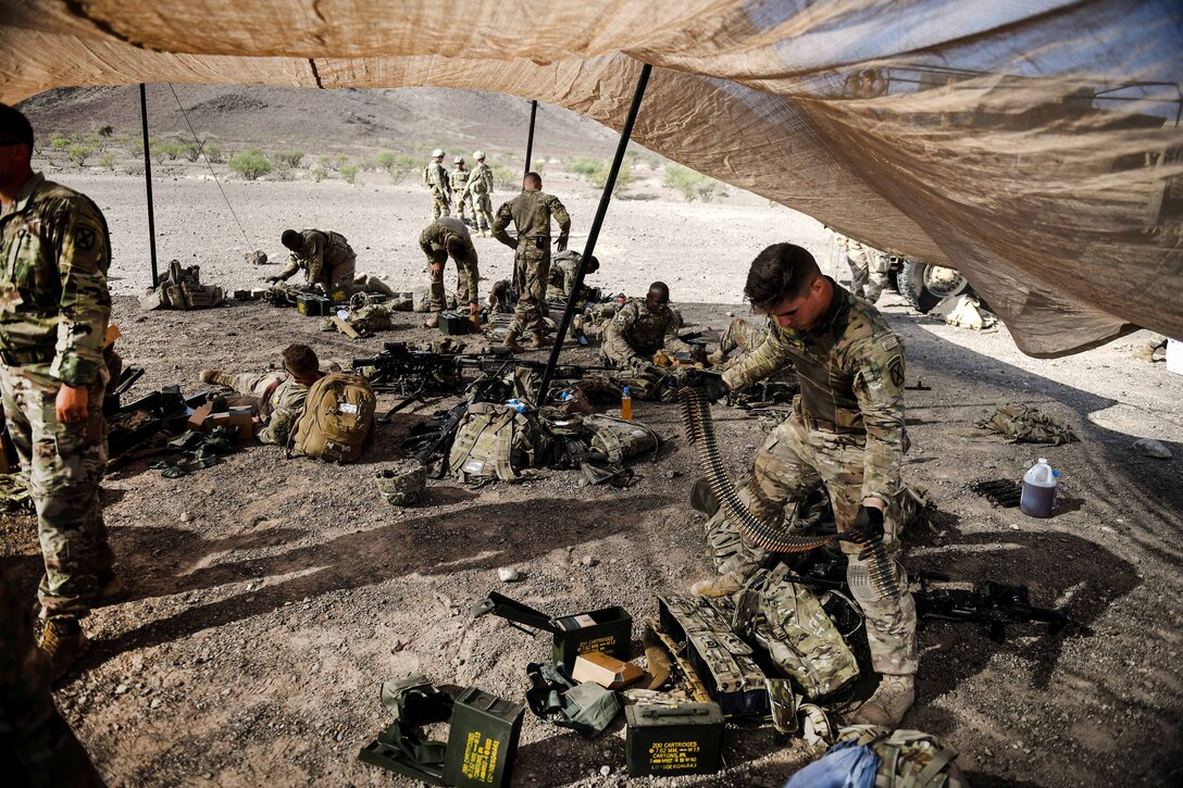Soldiers under a tarp prepare their weapons and equipment.