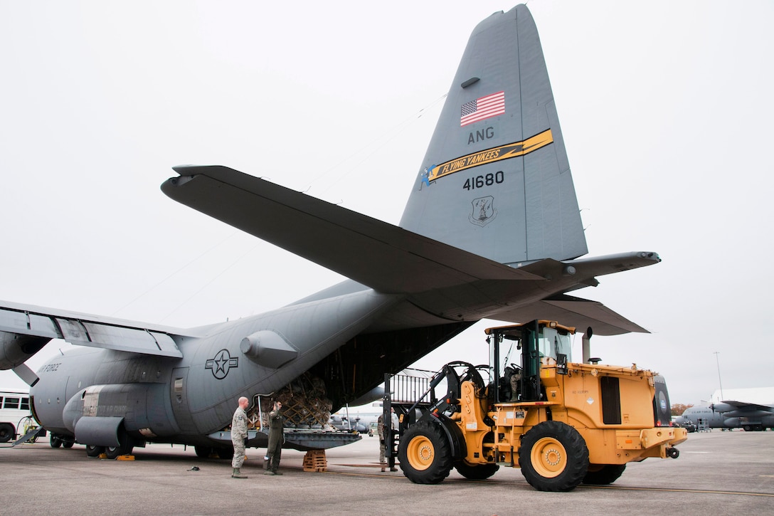 Guardsman guides a forklift operator loading gear onto a C-130 Hercules aircraft.