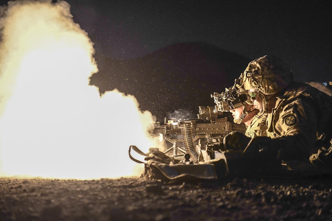 Soldiers crouching in a line fire weapons, creating a large fireball.