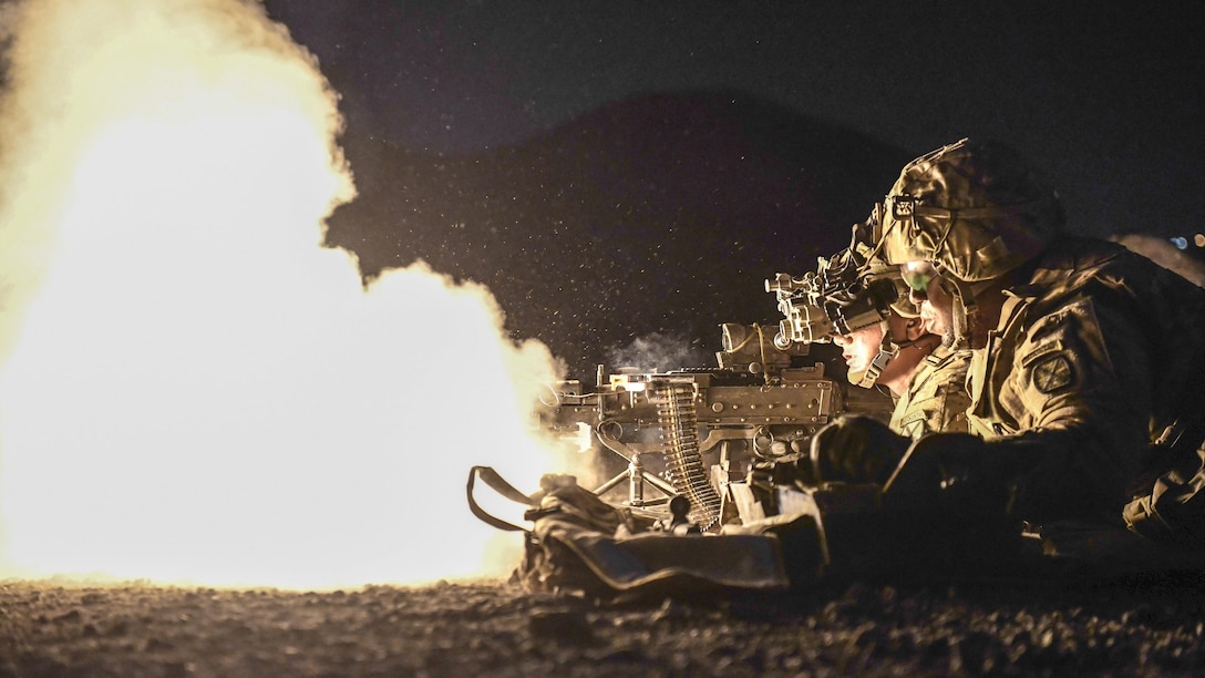 Soldiers crouching in a line fire weapons, creating a large fireball.