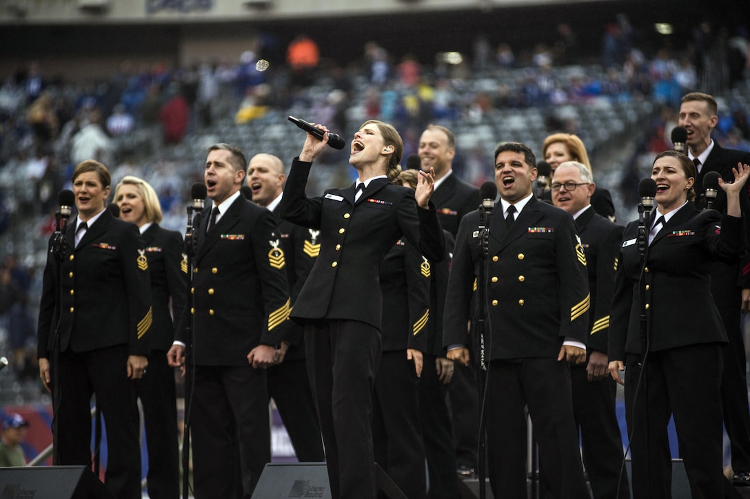 A group of sailors sing on the field at a stadium.