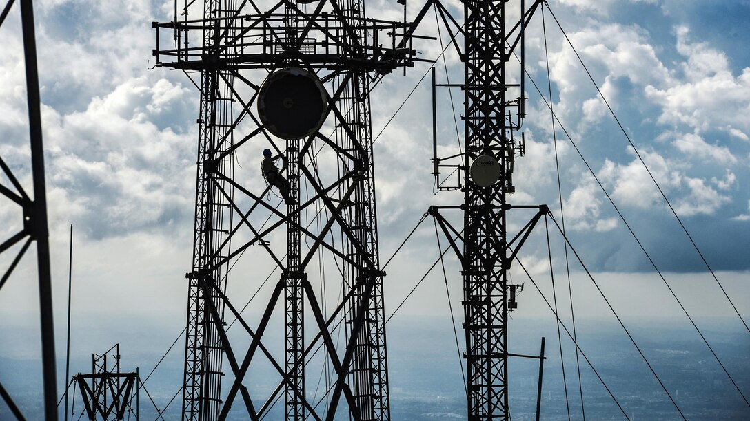 An airman, shown in silhouette, works on a cell tower.