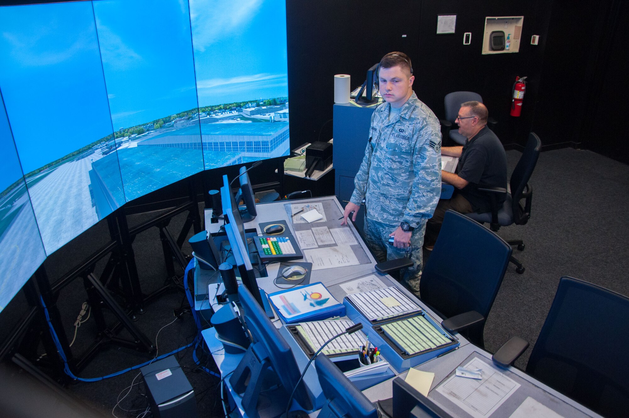 Senior Airman Zachary Cinnamon, 88th Operations Support Squadron air traffic controller, runs through an air traffic control scenario on Wright-Patterson's simulator as Jack Wilson, Air Traffic Control Tower Simulator administrator, operates the simulator behind him. The simulator allows controllers to train on complex air traffic control scenarios safely, preparing them to handle real-life operations. (U.S. Air Force photo/John Harrington)