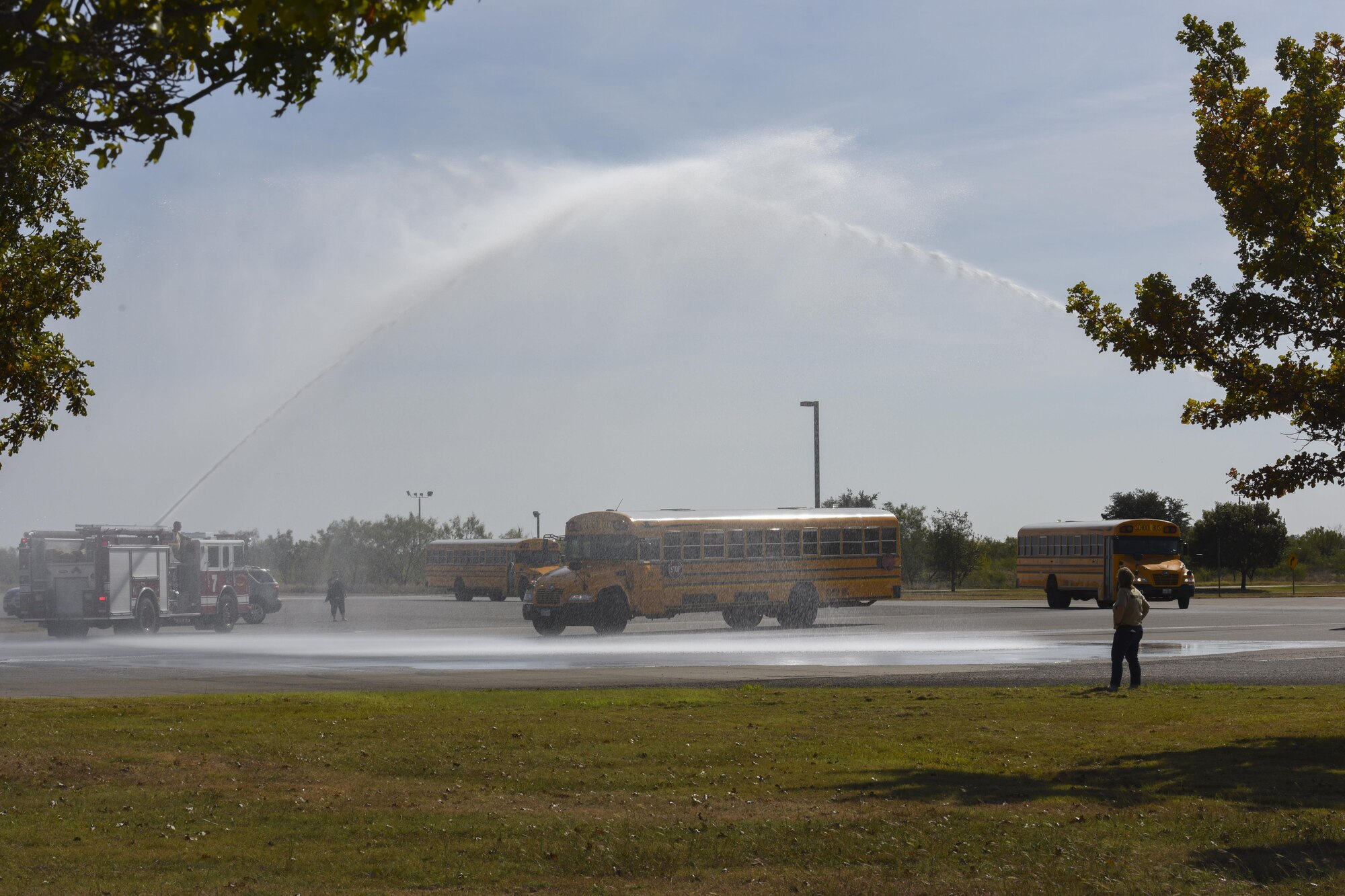 Buses carrying the children participating in Operation Kids Investigating Deployment Service are welcomed home by two streams of water from firetrucks at the Louis F. Garland Department of Defense Fire Academy on Goodfellow Air Force Base, Texas, Nov. 4, 2017. The kids experienced what a deployment may be like when a parent has to deploy. (U.S. Air Force photo by Airman 1st Class Zachary Chapman/Released)