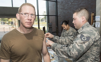 U.S. Air Force Staff Sgt. Jacob Radford, right, 628th Aerospace Medical Squadron allergy and immunizations technician, administers the annual flu shot to U.S. Navy Capt. Robert E. Hudson, left, Naval Support Activity Charleston commander, during a mobile flu line in the Joint Base Charleston Headquarters Building Nov. 7, 2017.
