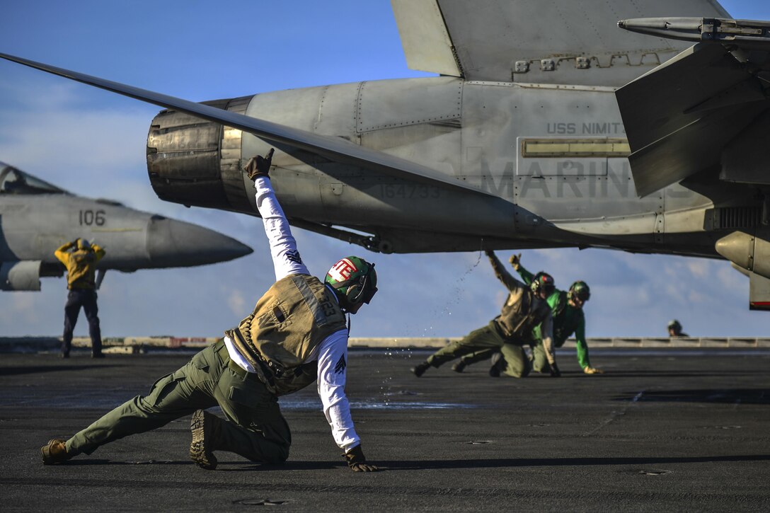 Three Marines kneeling on a flight deck hold their thumbs up on either side of an aircraft.