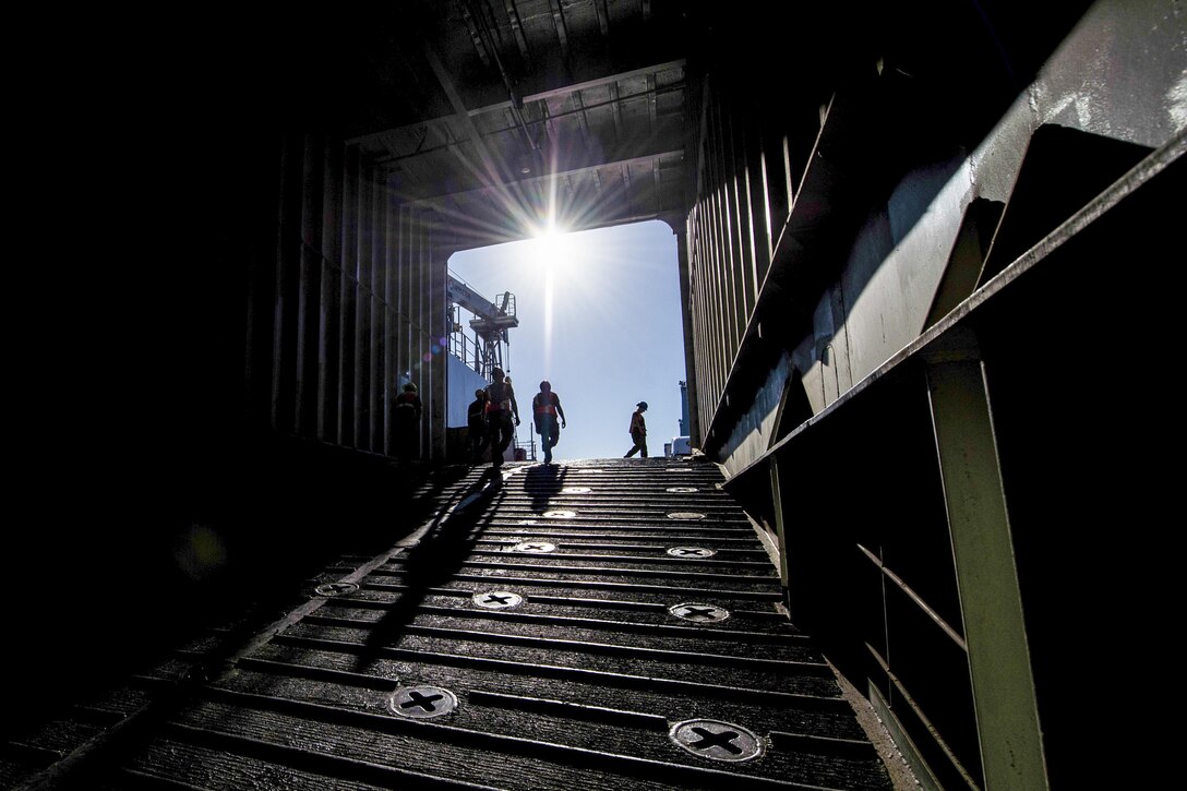 Blue sky and sunlight illuminate a dark metallic corridor leading out of a ship.