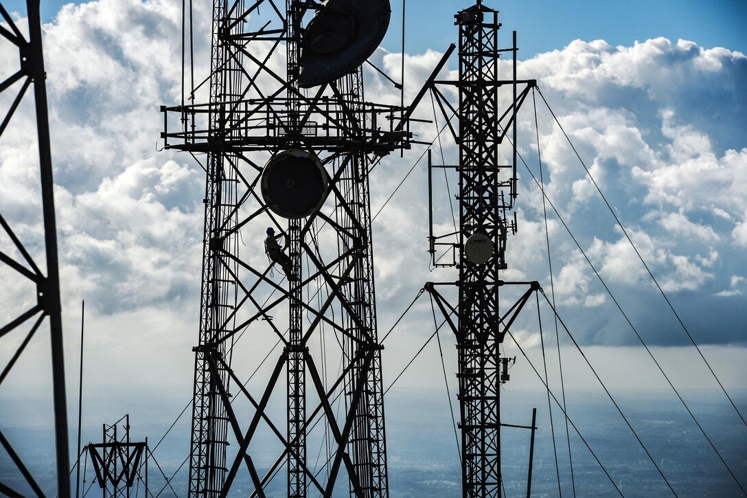 An airman, shown in silhouette, works on a cell tower.