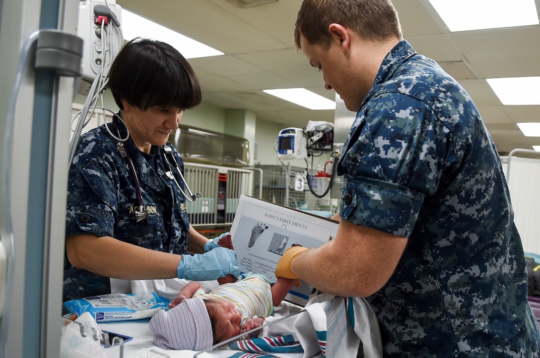 Two sailors take the footprint of a newborn baby.