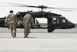 Two Soldiers carry another on a litter towards a helicopter.