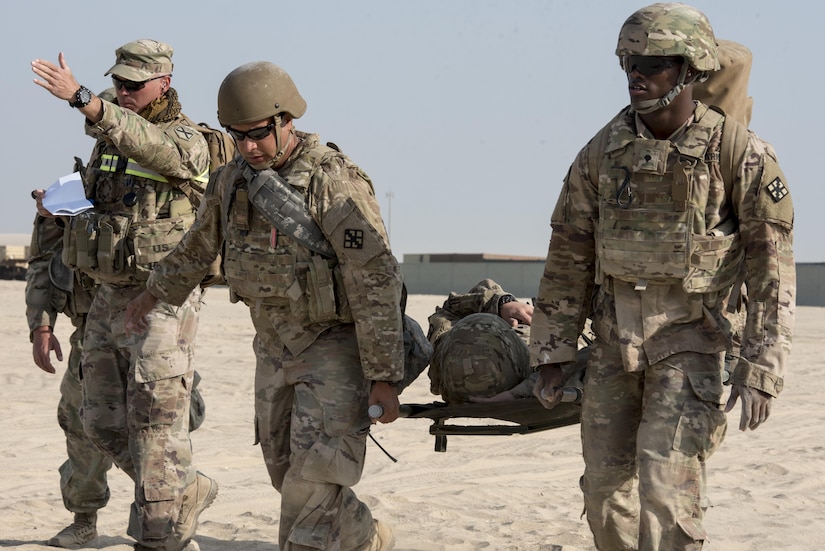 Two Soldiers carry another on a litter while a third Soldier instructs.