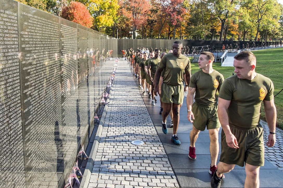 Marines in running wear walk in a line along the Vietnam Veterans Memorial, reading the names on the wall.