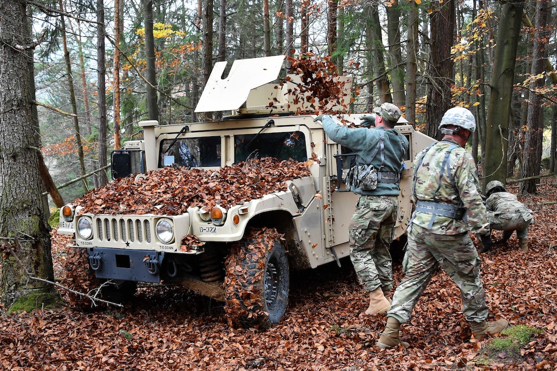 Soldiers toss leaves onto a Humvee.