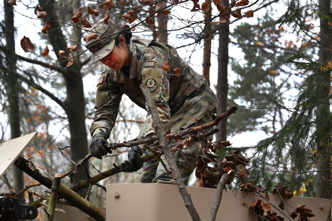 A soldier puts branches and leaves onto a Humvee.