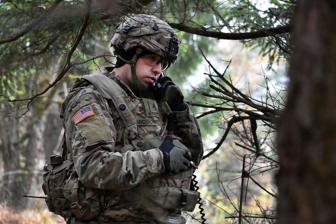 A soldier talks on a radio in the forest.