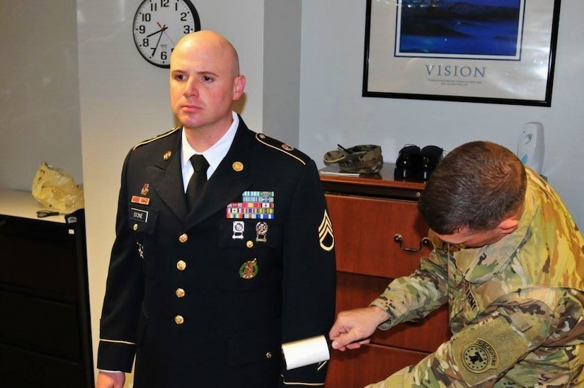 Soldier in camouflage lint rolls a soldier in dress uniform