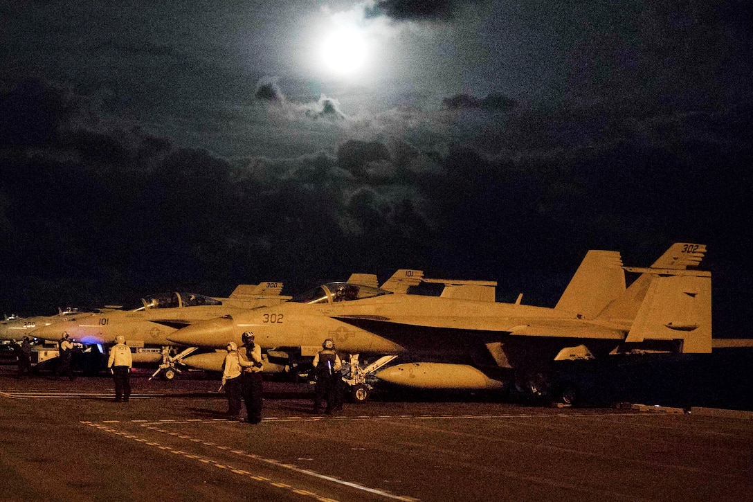 Sailors prepare several fighter jets during night flight deck operations on an aircraft carrier.