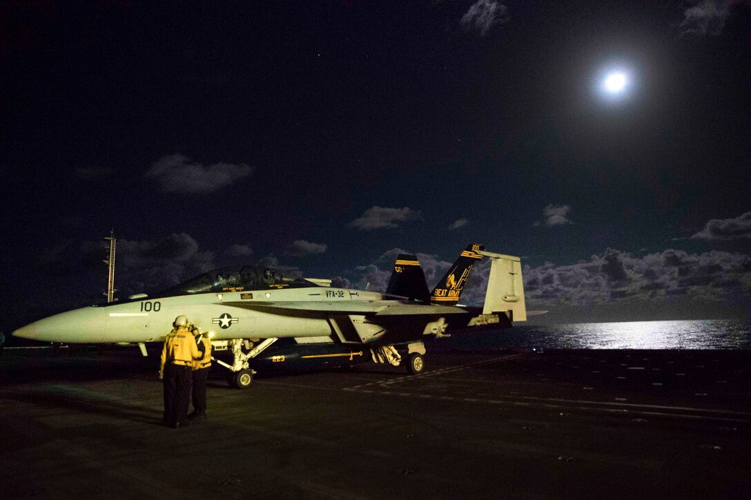 A fighter jet waits to be parked after night flight operations on an aircraft carrier.