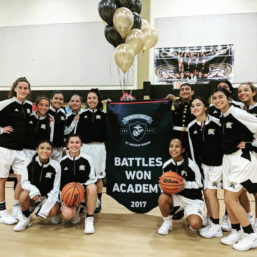 Shania Esquivel, a senior at John Paul II High School, holds the Battles Won banner with Staff Sergeant Lucas Leal during a half-time presentation at a home game November 7, 2017. Esquivel was one of the 100 juniors selected to attend the inaugural Semper Fidelis All-American Program Battles Won Academy.