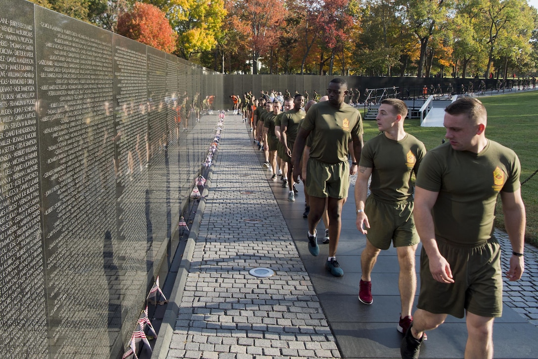 Marines in running wear walk in a line along the Vietnam Veterans Memorial, reading the names on the wall.
