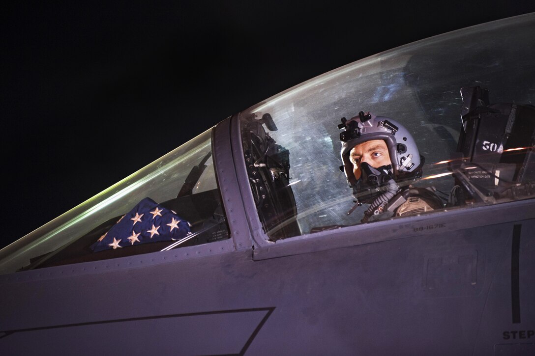 A pilot looks out the cockpit of an aircraft with a folded American flag in the window.