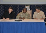 Three flag officers facing viewer at table, signing document.