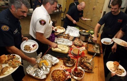 Several fire fighters gather around the table at their fire station to enjoy a home-cooked Thanksgiving Day meal.
