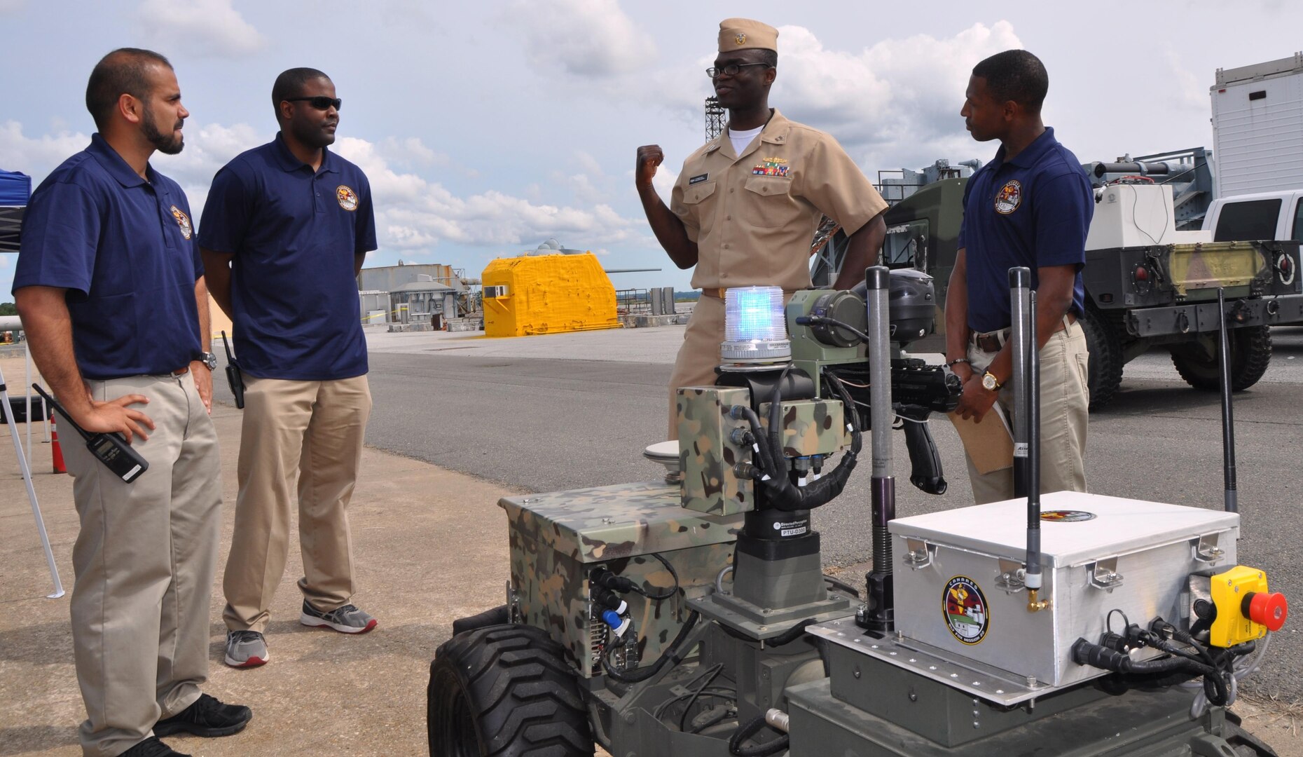 IMAGE: DAHLGREN, Va. (Sept. 12, 2017) - Navy Sly Fox Mission 22 junior scientists and engineers brief Lt. Akwasi Fosu on the new capabilities of Weaponized Autonomous System Prototype (WASP) after a demonstration held at Naval Surface Warfare Center Dahlgren Division.  The seven-member Mission 22 team integrated WASP with an unmanned aerial vehicle (UAV) to provide an aerial perspective for increased situational awareness. Navy civilian and military personnel witnessed the Mission 22 demonstration of the Collaborative Aerial Network for the Autonomous Remote Engagement System – fully-integrated with the UAV, WASP, and a command and control station while detecting, tracking, and engaging targets on the Potomac River Test Range. Standing left to right are Jamshaid "JD" Chaudhry, Allen Woods, Fosu, and Chris Toney.