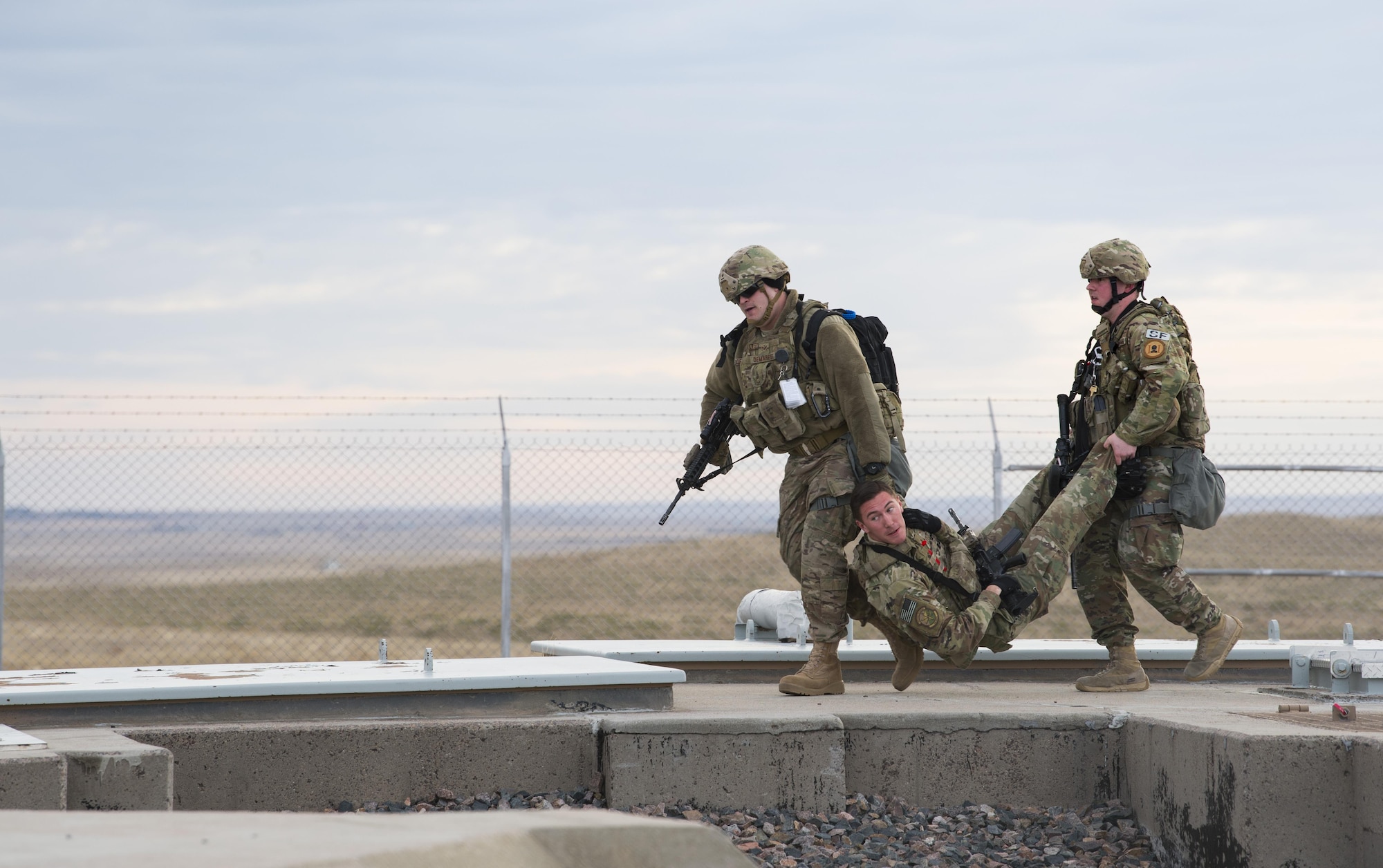 Two airman carry an airman across the ground