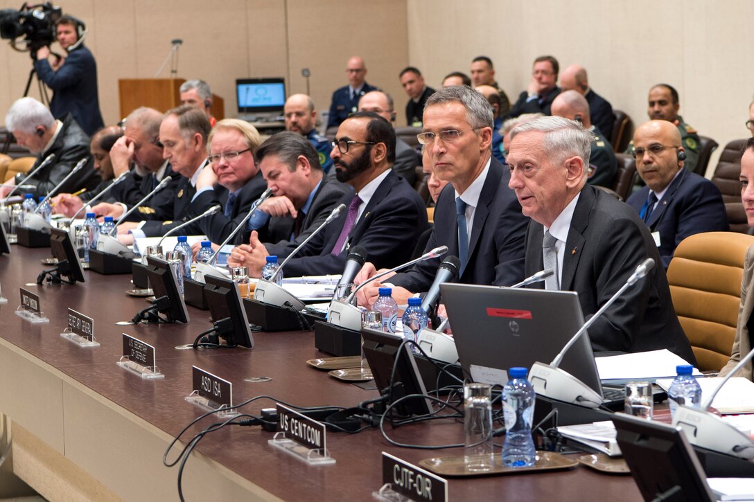 Defense Secretary Jim Mattis speaks into a microphone while sitting next to others.