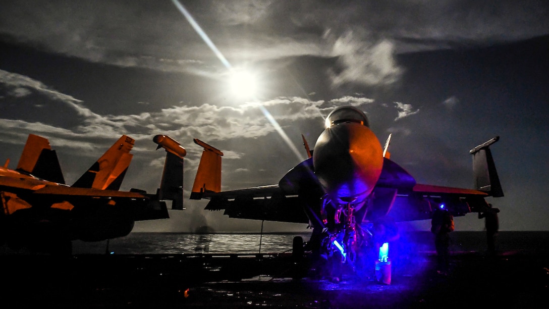 Aircraft sit on the deck of an aircraft carrier at night.