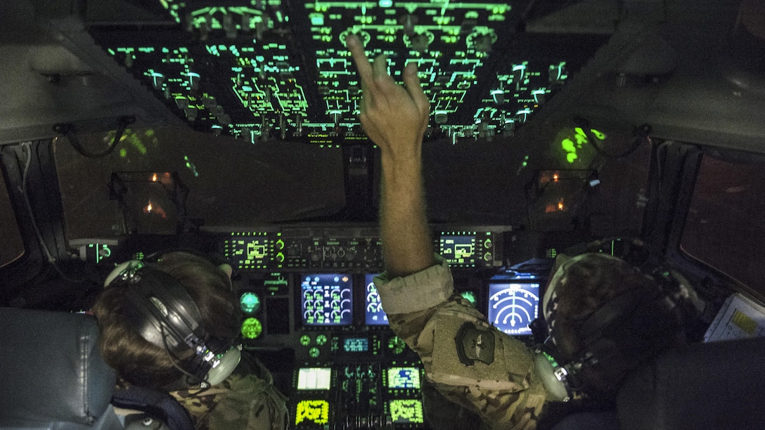 Pilots work overhead controls in an aircraft at night.