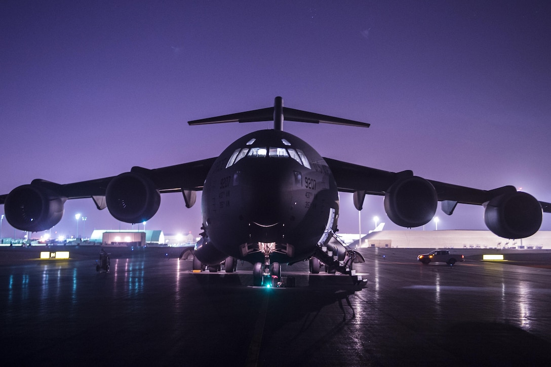 A military aircraft sits on a runway at night with a purple sky in the background.