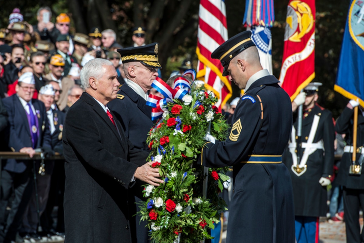 Vice President Mike Pence places a wreath on a stand with the assistance of a service member.