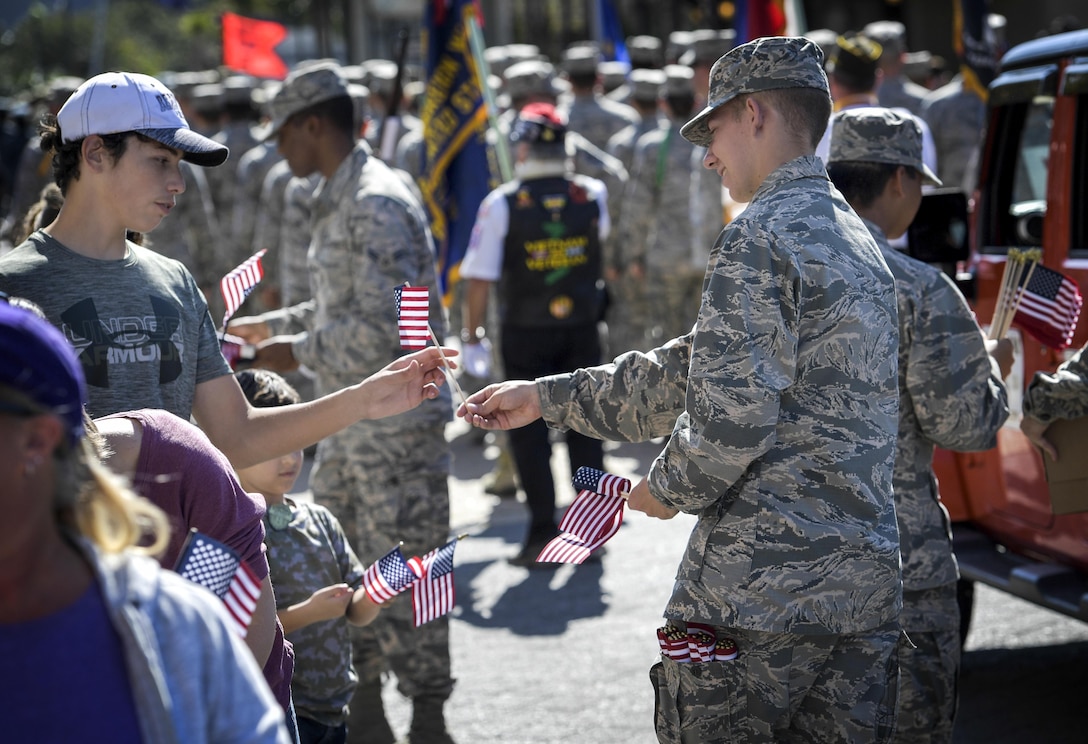 An airmen hands a small flag to a young man.