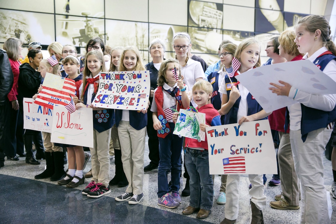 Veterans, active duty military and civilians hold signs welcoming  wounded warriors.
