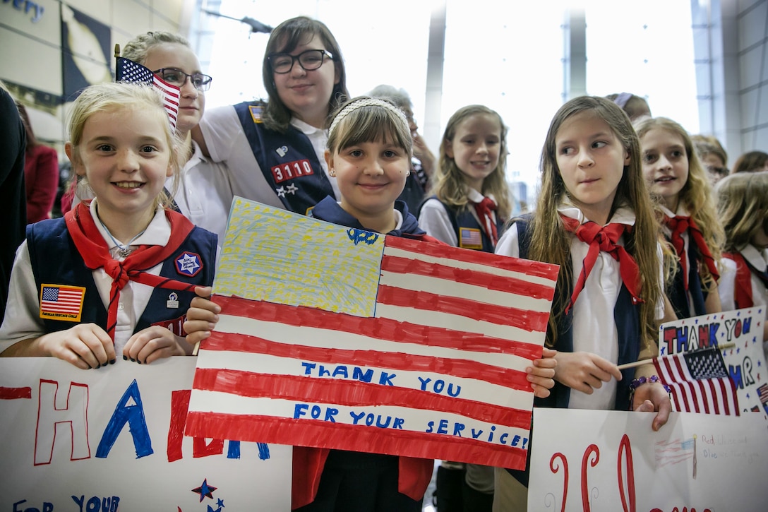 Students hold signs welcoming wounded warriors at an airport.